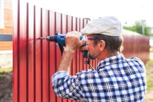 Un anciano con un taladro construye una valla de metal