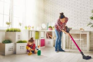 Una mujer joven y una niña están limpiando el polvo y aspirando el suelo