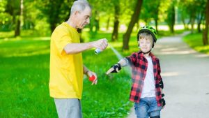 Viejo hombre es sparying insecto repelente en el brazo del niño