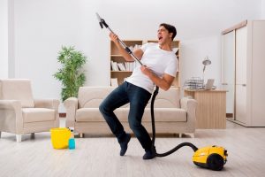 Hombre felizmente limpiando casa con aspiradora