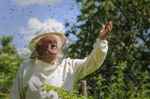 Un apicultor se encuentra en un lugar natural, y las abejas pululan a su alrededor.