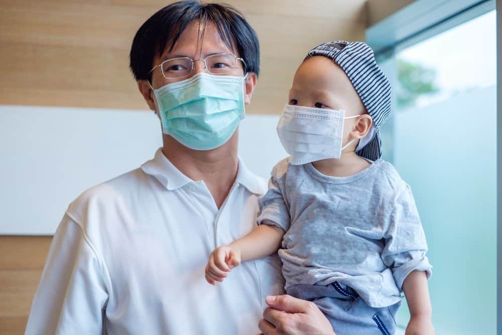 Un asiático padre sosteniendo su hijo en brazos con máscaras en su rostros