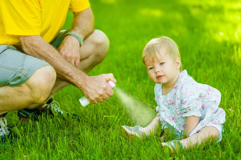 Padre usando spray de mosquitos en la pierna de la niña pequeña